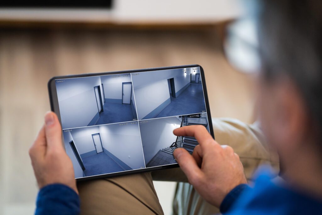 Pentest em aplicativos de monitoramento: imagem de pessoa verificando quatro feeds de câmera de segurança CCTV em um tablet, ilustrando a vigilância remota e a superfície de ataque que requer análise de API e pentest especializado